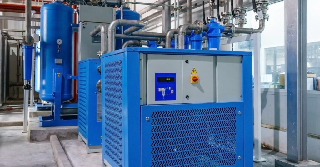 Two blue industrial-sized air compressors sitting in the corner of a factory with metal piping coming off of them.